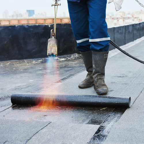 A person is laying modified bitumen roofing with a torch.