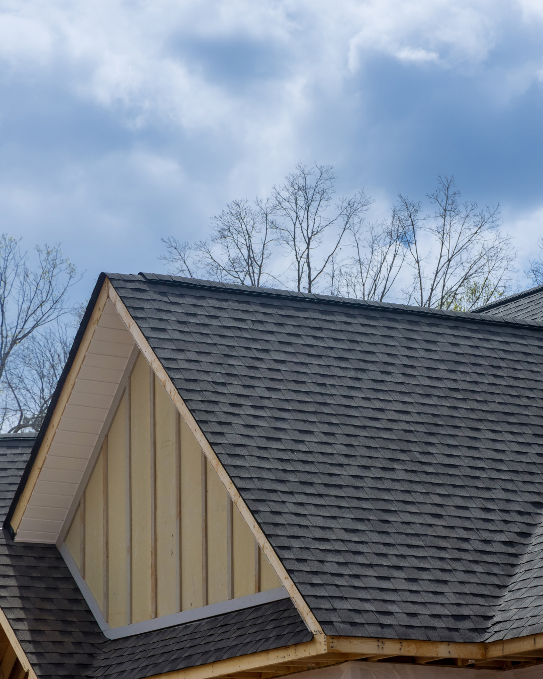A house with a gray asphalt shingle roof and a blue sky in the background.