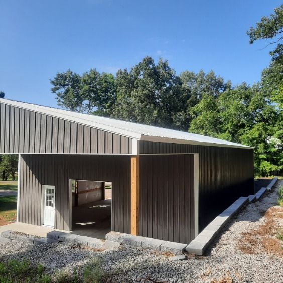 A large metal building with a white roof is surrounded by trees.