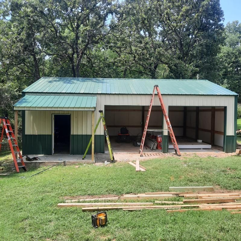 A metal building with a green roof is being built in a grassy field.