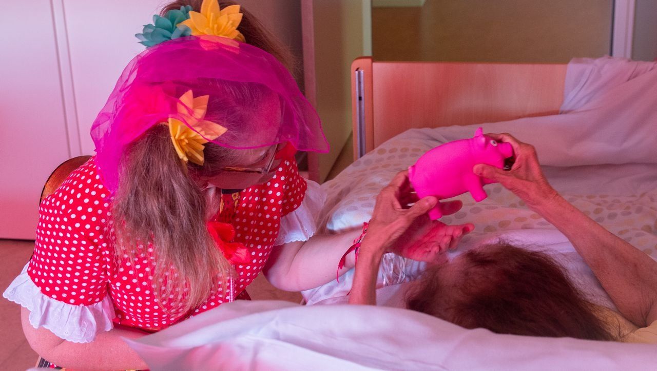 zorgclown Aagje, clown Aagje, zorgclown, clown, contactclown, contactclown Aagje, contact, mevrouw op bed , doekje op hoofd clown en varkentje vast