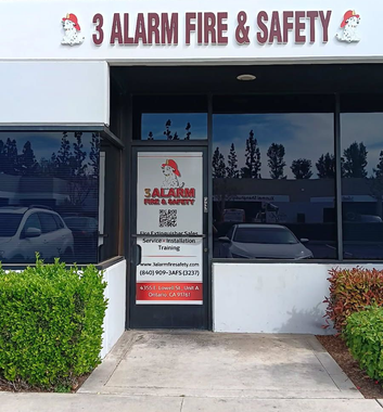 The storefront of 3 Alarm Fire & Safety, Ontario, CA with a branded glass door, signage, and greenery in front of the building.