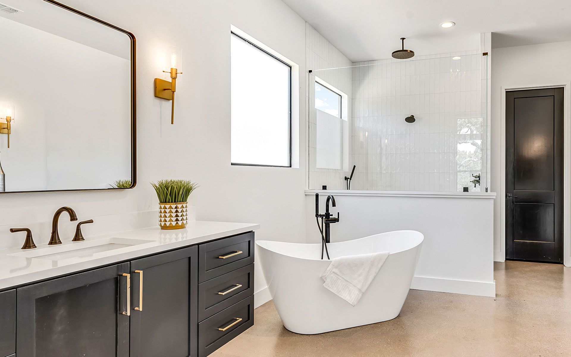 Modern bathroom with a dark gray vanity, white bathtub, and gold accents.