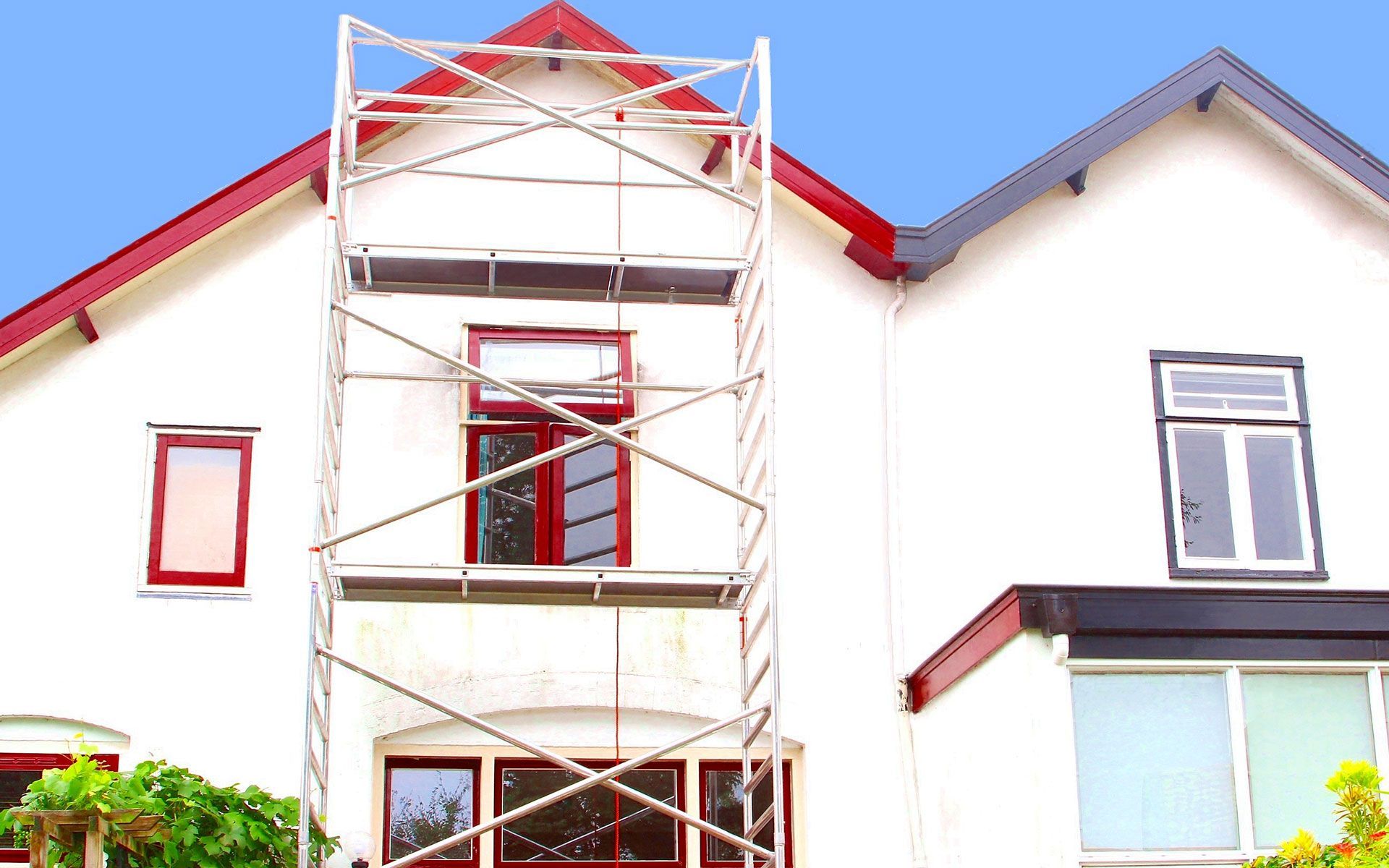 Scaffolding next to a white house with red trim and windows, under a blue sky.
