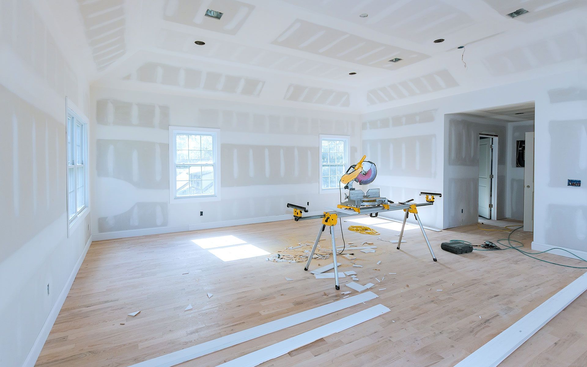 Interior of a room under construction with drywall, wooden flooring, and a saw.