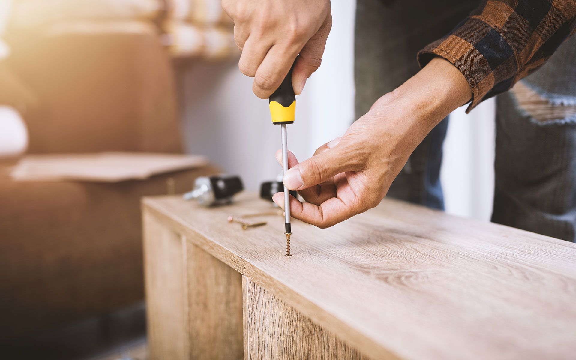 Person using a yellow and black screwdriver to assemble a wooden cabinet indoors.