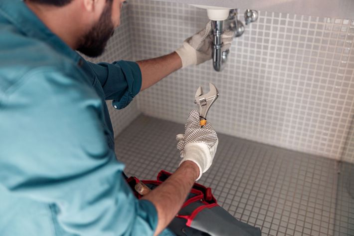 A man is fixing a sink in a bathroom with a wrench.