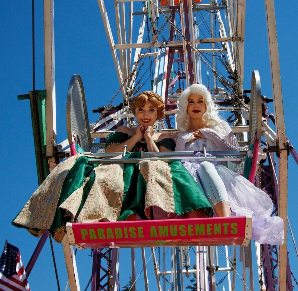 Two dolls are riding a ferris wheel that says paradise amusements