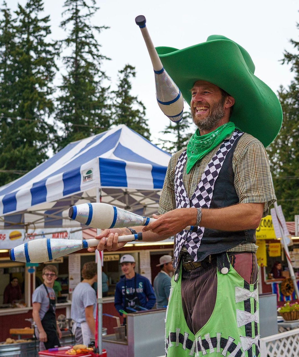 A man in a green cowboy hat is juggling clubs