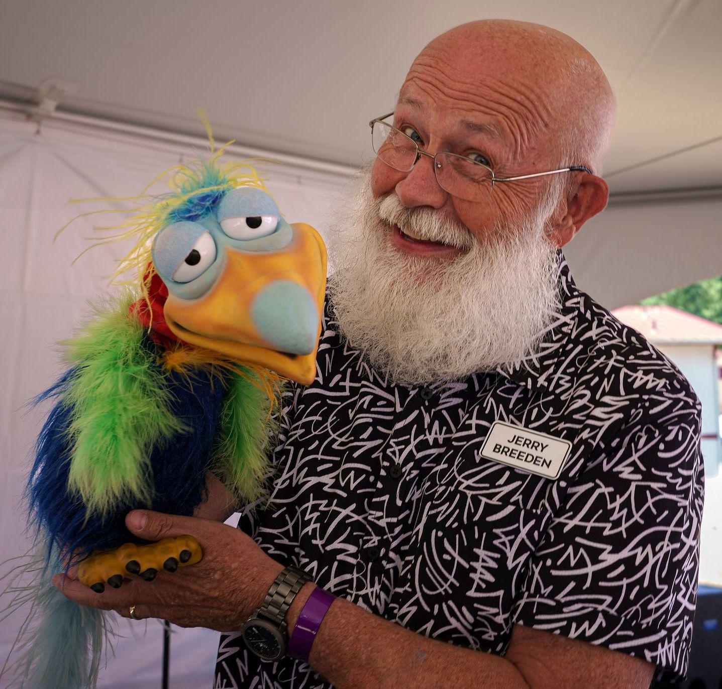 A bald man with a beard is holding a colorful stuffed bird