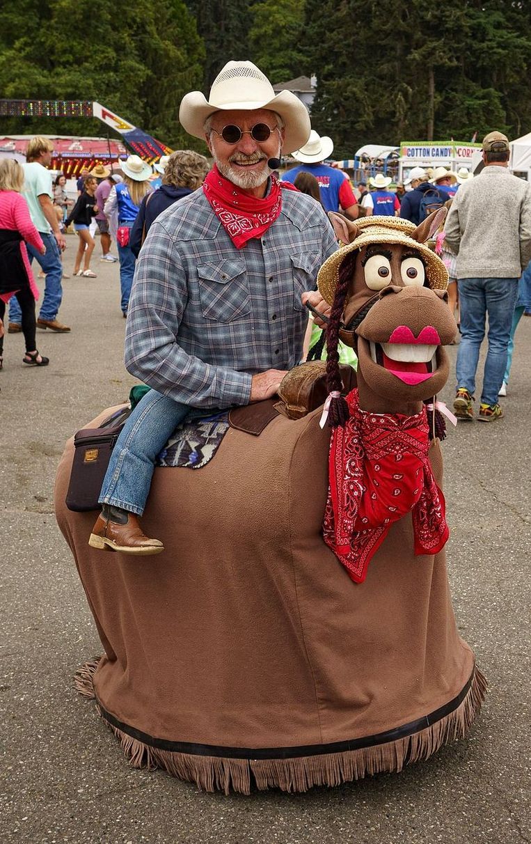 A man dressed as a cowboy is riding a stuffed horse.