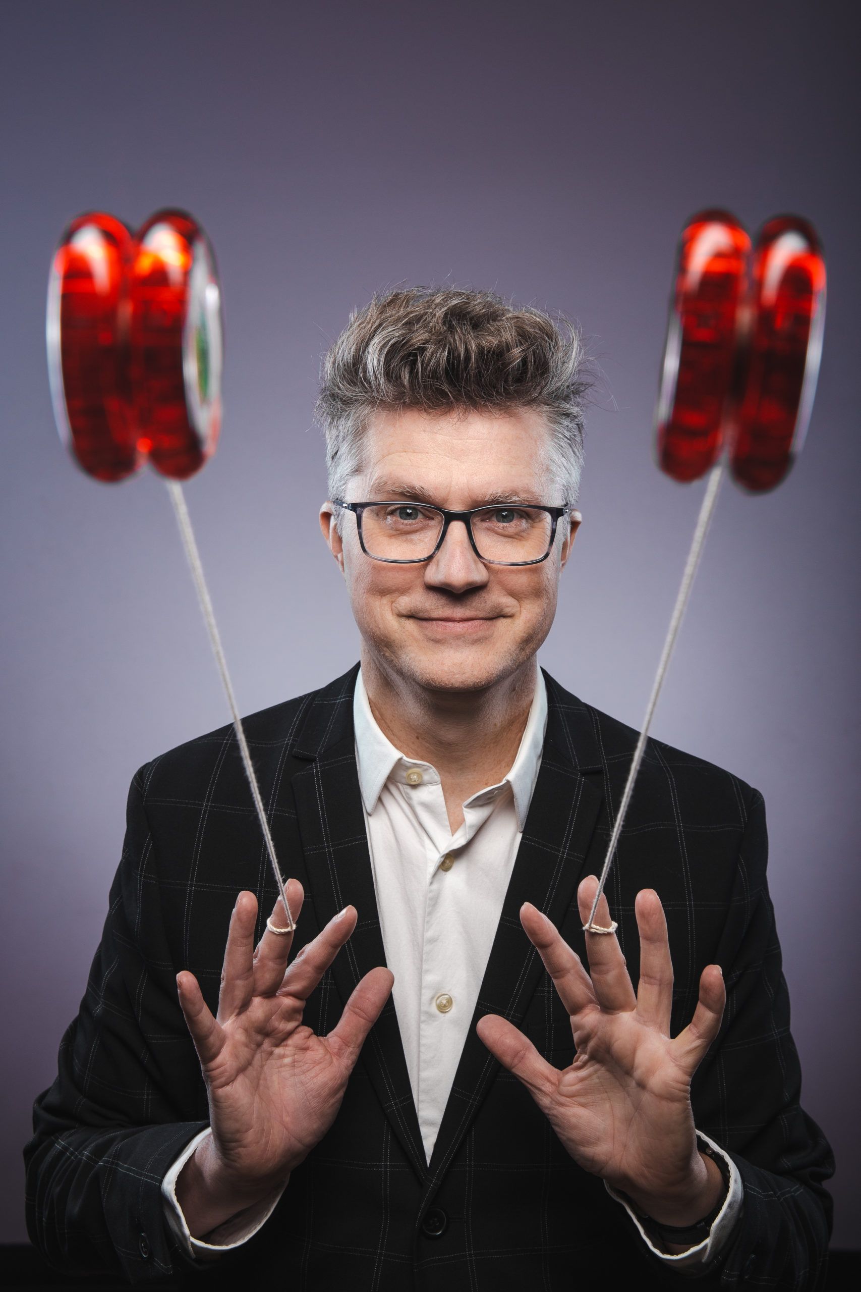 A man in a suit is holding two red balloons in his hands.