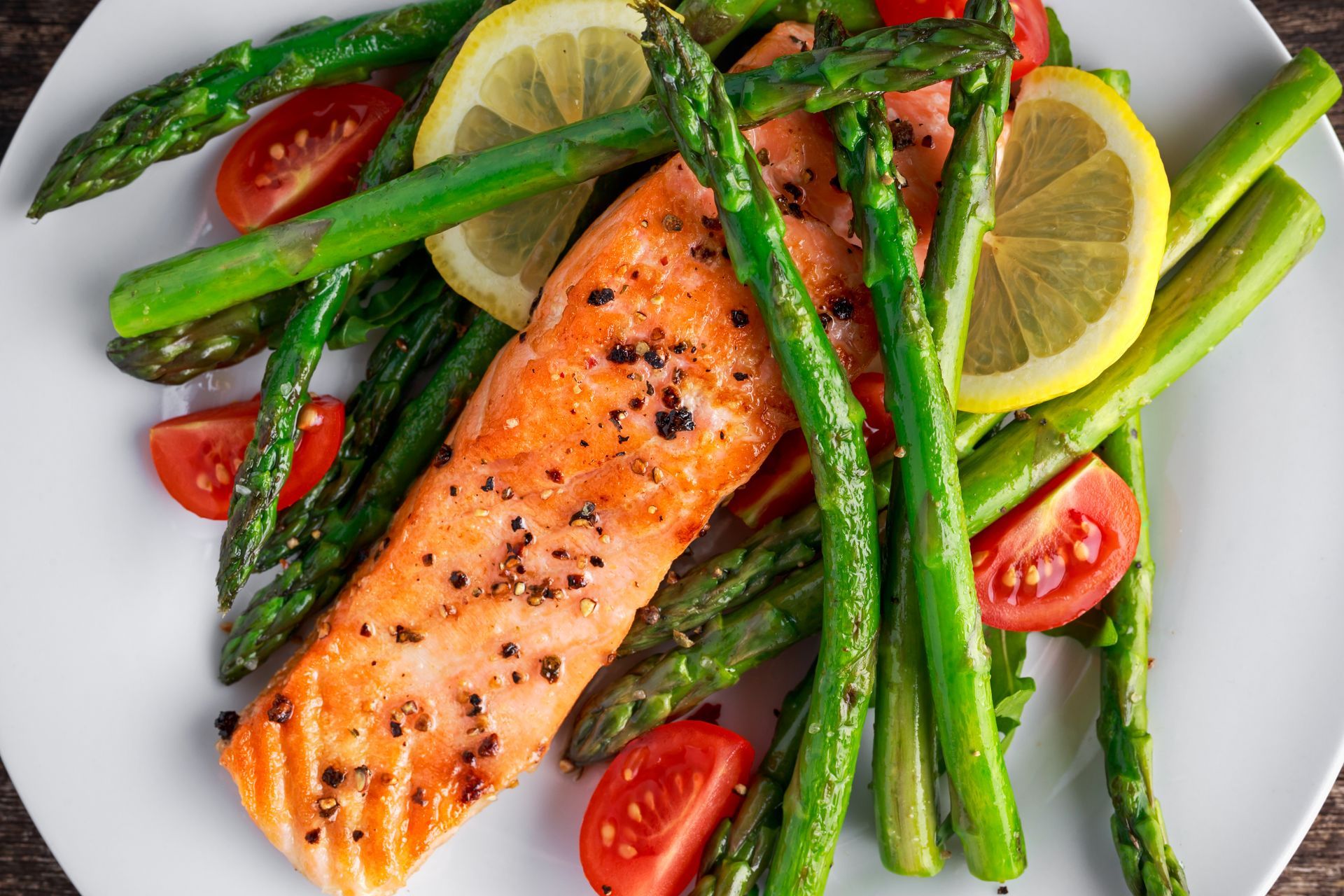 A white plate topped with salmon , asparagus , tomatoes and lemon slices.