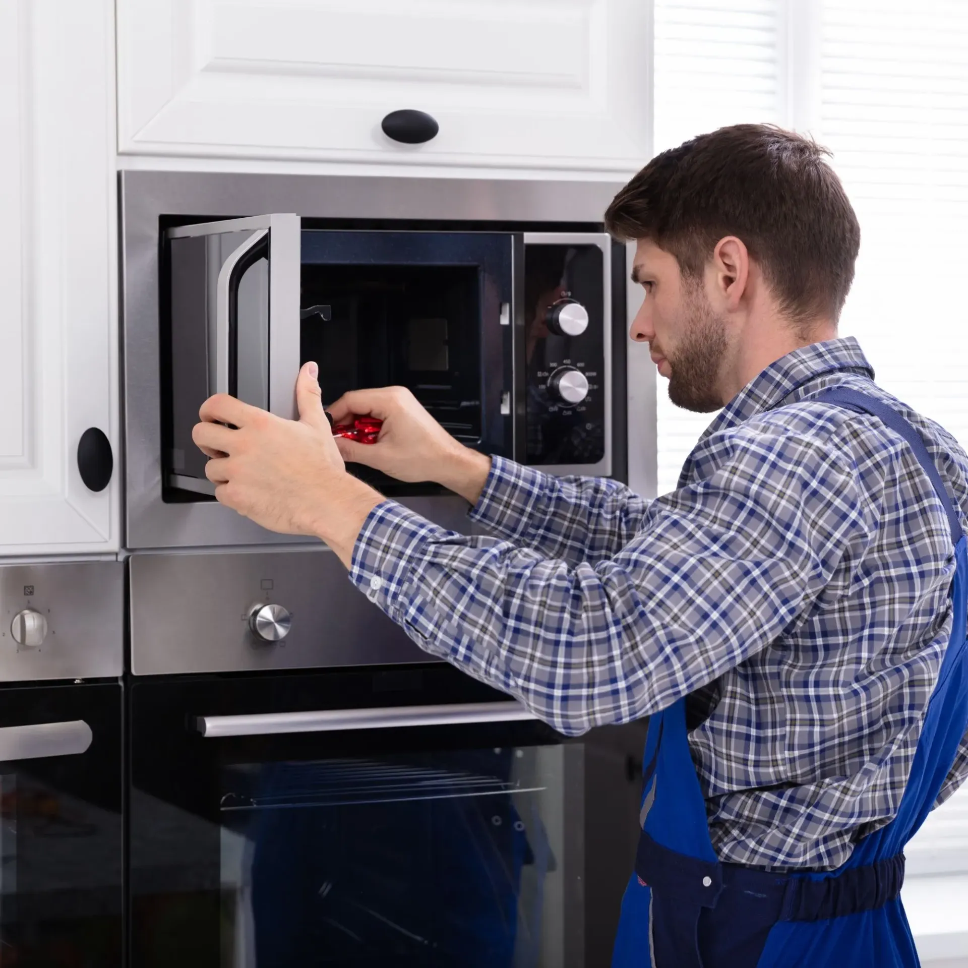 Davis Appliance & Tool Repair - A man is fixing a microwave oven in a kitchen.