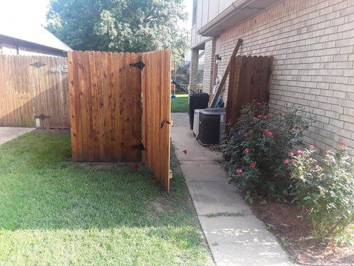 A wooden fence is sitting in the backyard next to a brick building.