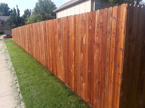 A wooden fence surrounds a lush green lawn in front of a house.