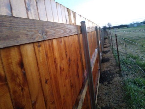 A wooden fence with a barbed wire fence in the background.