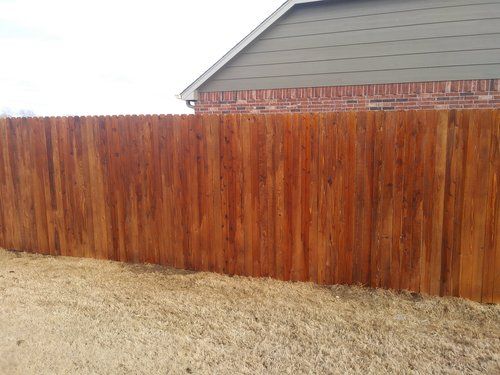 A wooden fence is in front of a brick house.