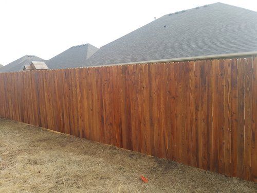 A wooden fence in a backyard with a house in the background.
