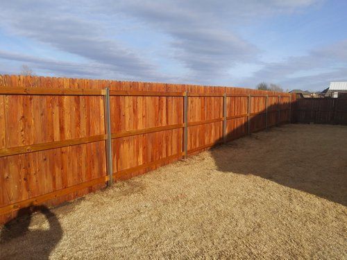 A wooden fence surrounds a gravel area in a backyard.
