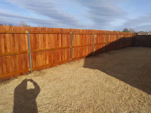 A person is taking a picture of a wooden fence in a backyard.