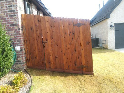 A wooden fence is sitting in the grass in front of a brick house.