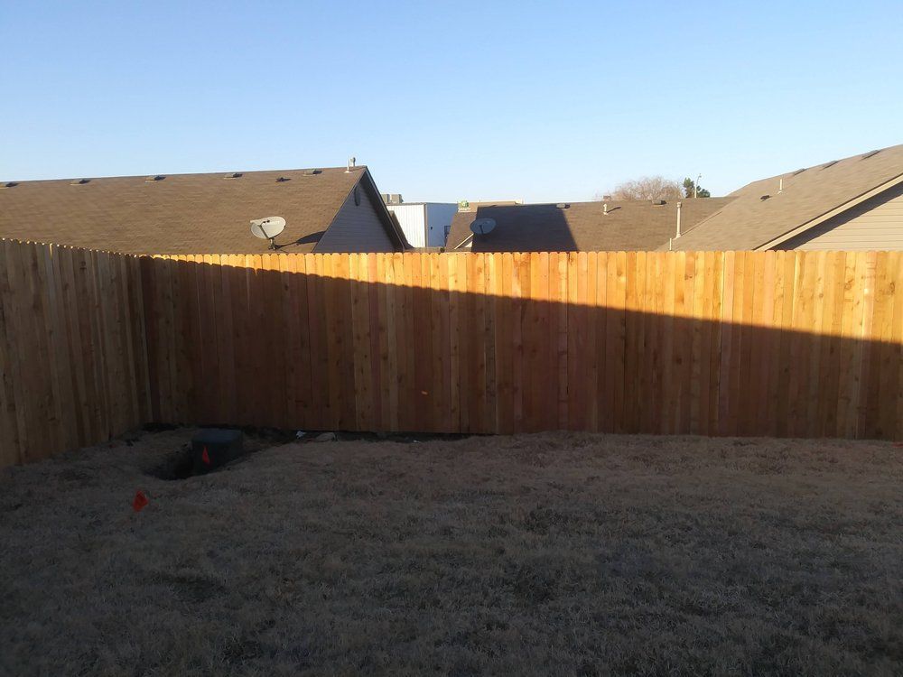 A wooden fence surrounds a backyard with houses in the background