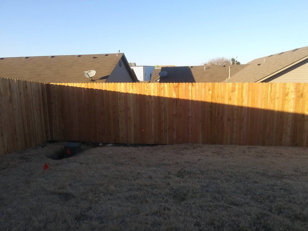 A wooden fence surrounds a backyard with houses in the background