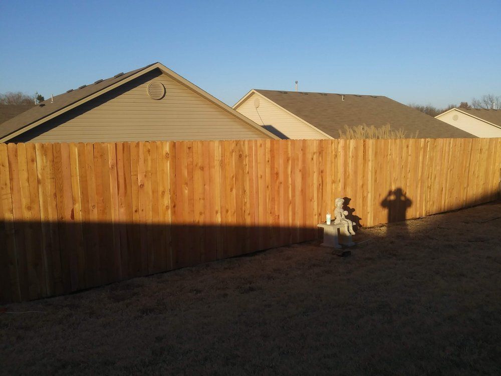 A wooden fence surrounds a backyard with houses in the background