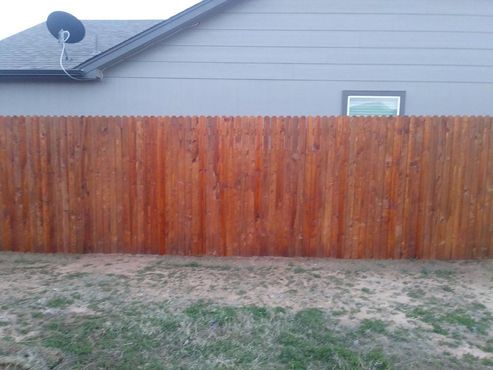 A wooden fence is in front of a house with a satellite dish on the roof.
