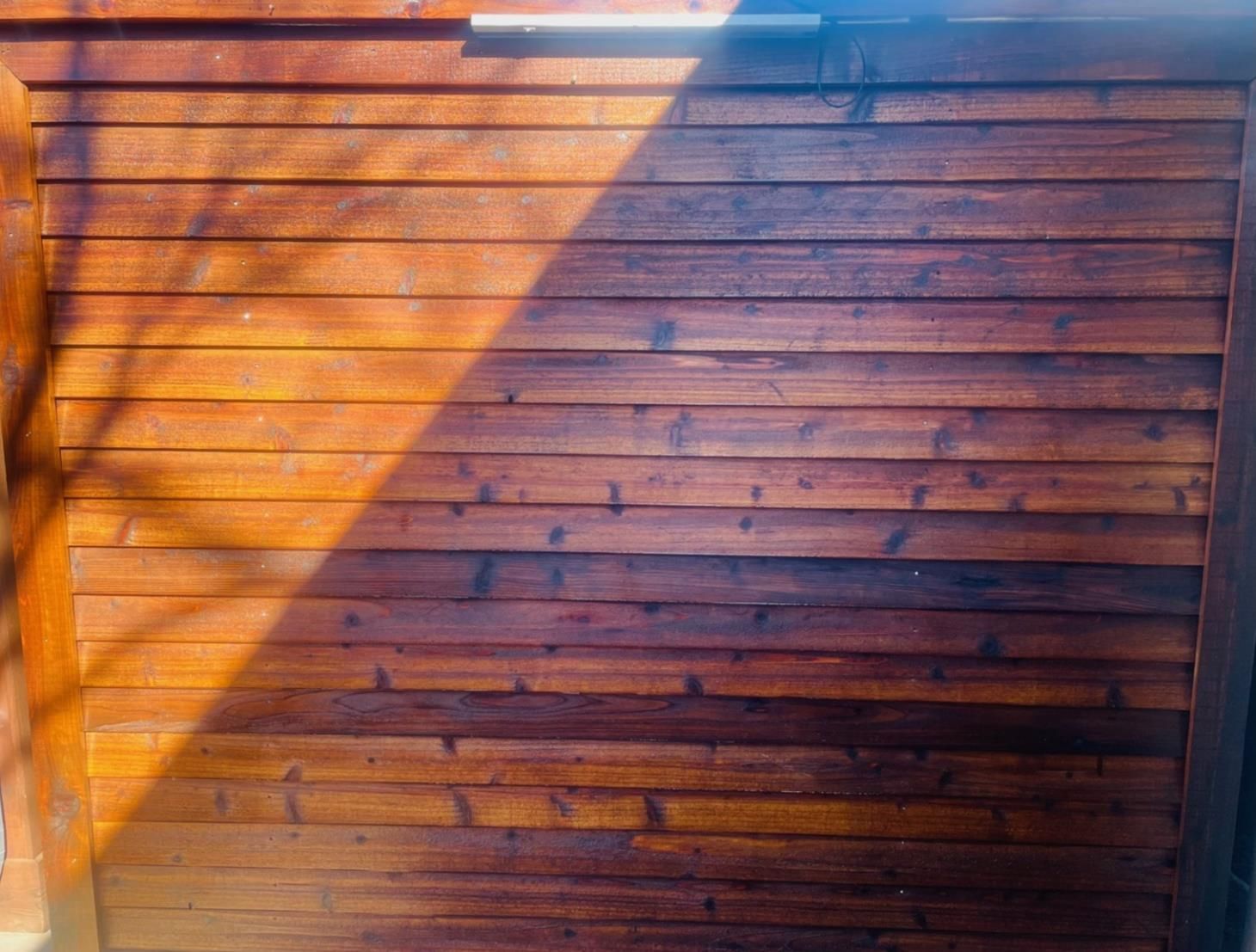 A close up of a wooden wall with a tree shadow on it.
