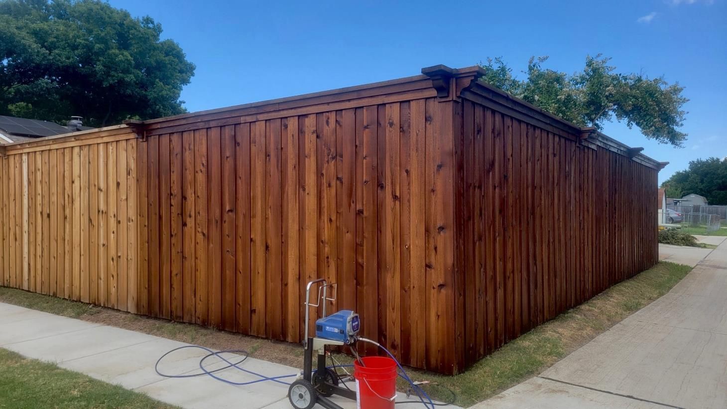 A wooden fence is being painted with a sprayer.