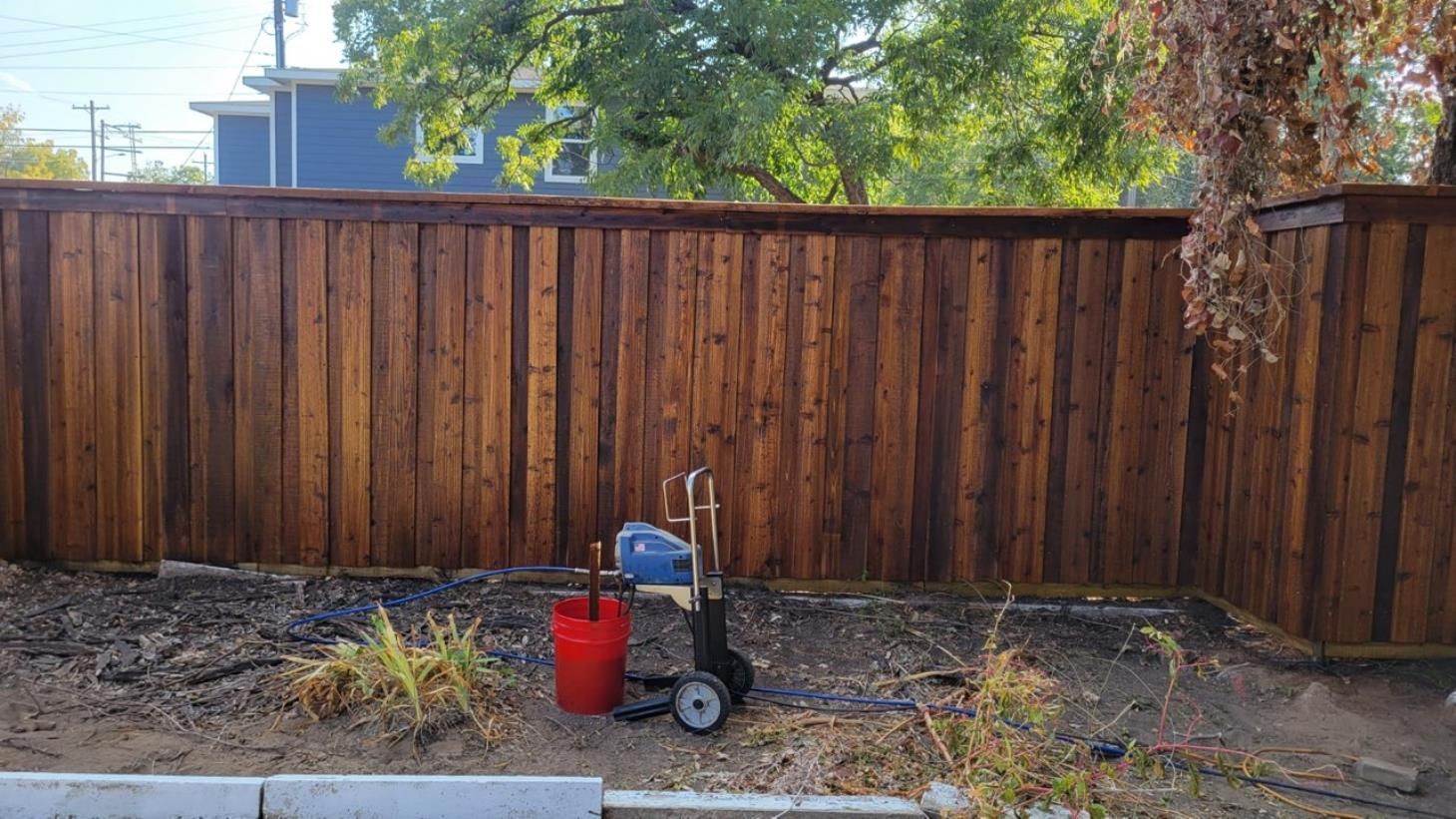 A wooden fence with a bucket and a vacuum cleaner in front of it.