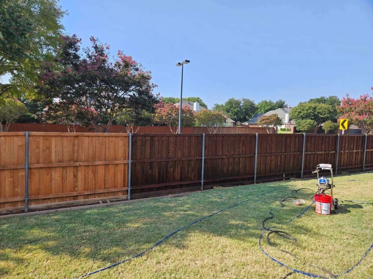 A wooden fence is being cleaned in a backyard with a pressure washer.