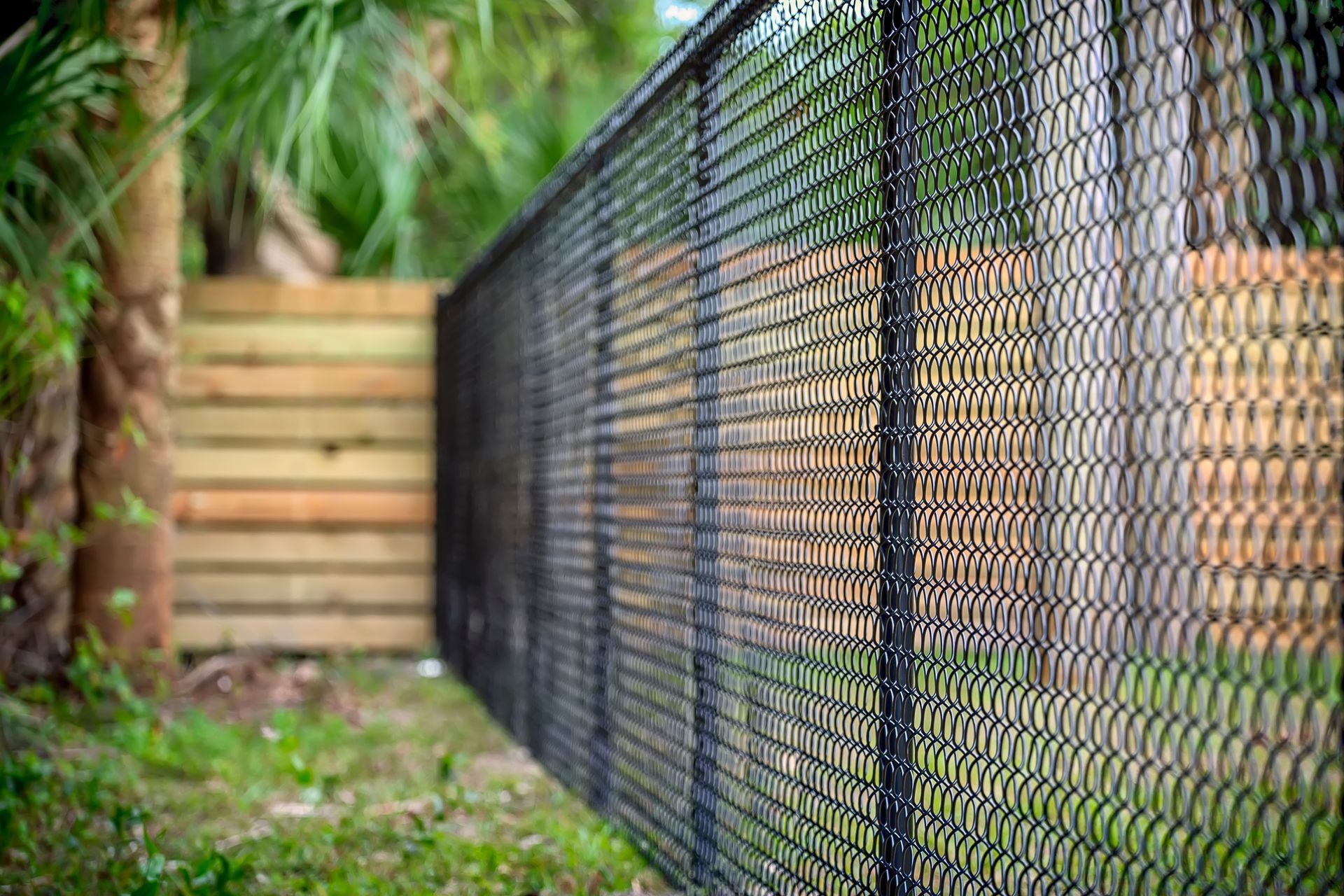 A close up of a chain link fence with a wooden fence in the background.