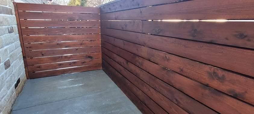 A wooden fence surrounds a concrete floor next to a brick wall.