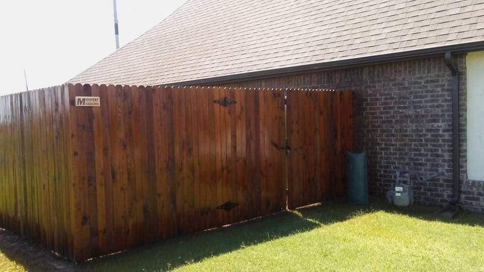 A wooden fence is in the backyard of a brick house.
