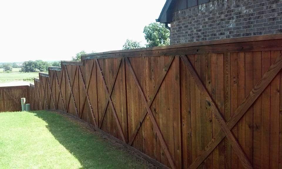 A wooden fence surrounds a lush green yard in front of a brick building.