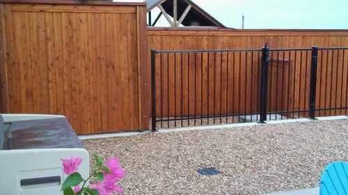 A wooden fence with a black metal railing is surrounded by gravel and flowers.