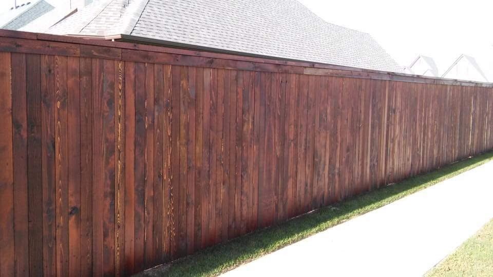 A wooden fence is sitting next to a sidewalk in front of a house.
