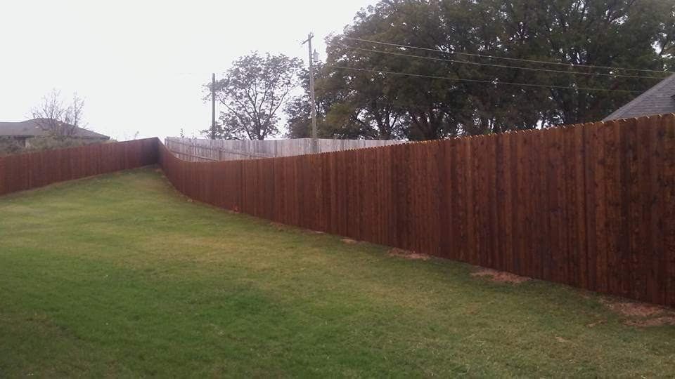 A long wooden fence surrounds a lush green yard.