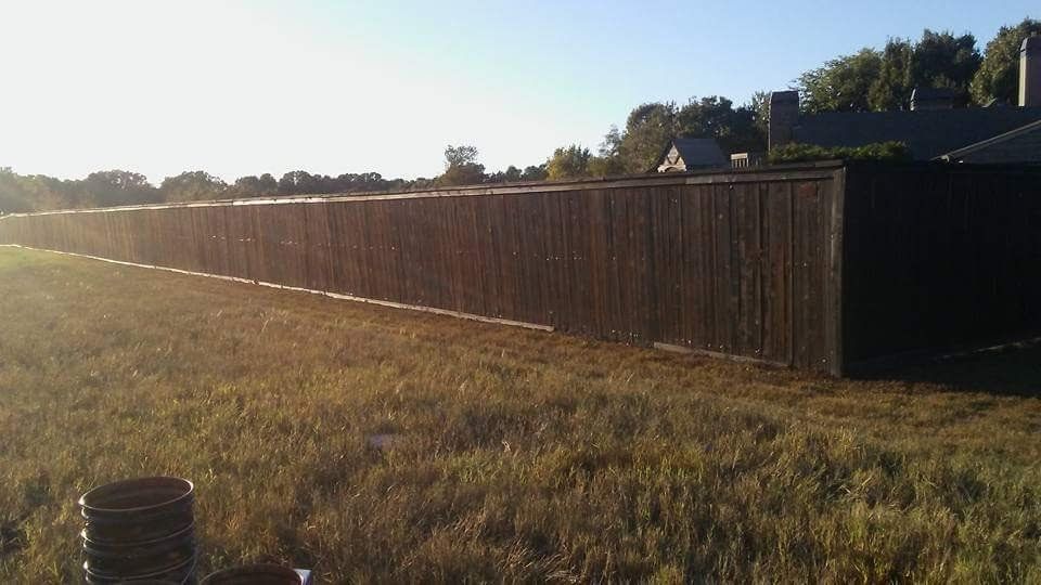 A long wooden fence is in the middle of a grassy field.