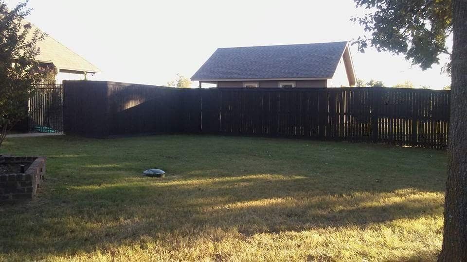A backyard with a fence and a house in the background
