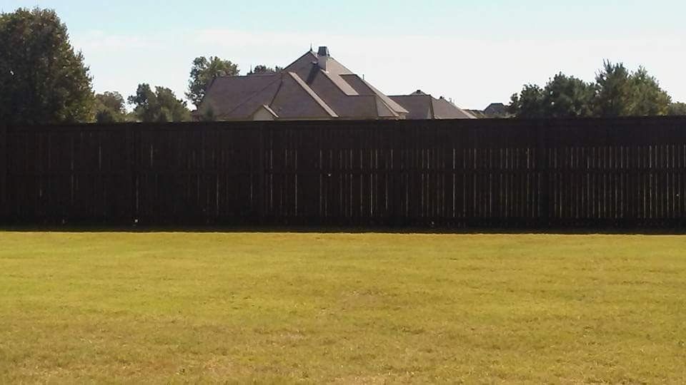 A fence surrounds a lush green field with a house in the background.