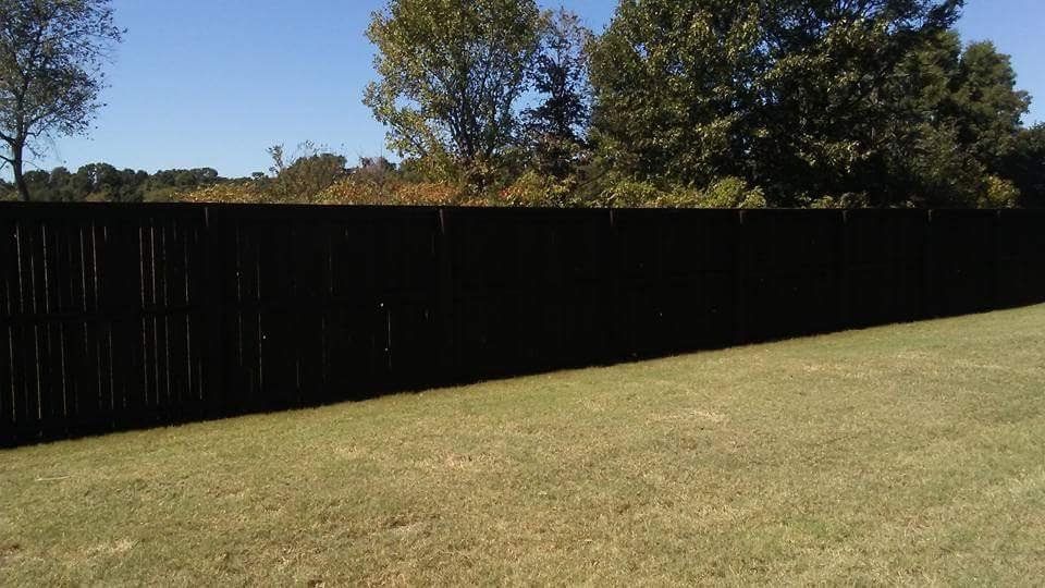 A black wooden fence surrounds a lush green field.
