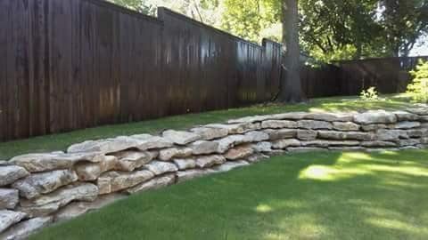 A stone wall in a backyard next to a wooden fence.