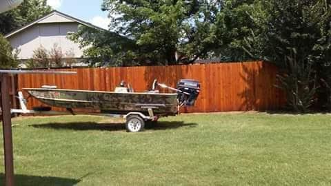 A boat is on a trailer in a grassy yard next to a wooden fence.