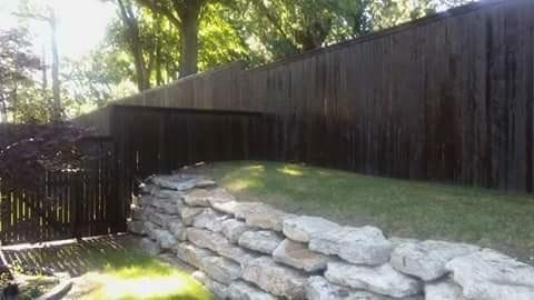 A wooden fence surrounds a rock wall in a backyard.