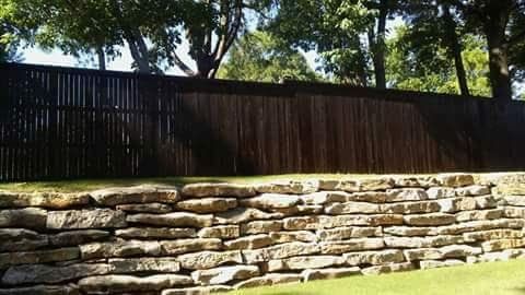 A stone wall with a wooden fence in the background.