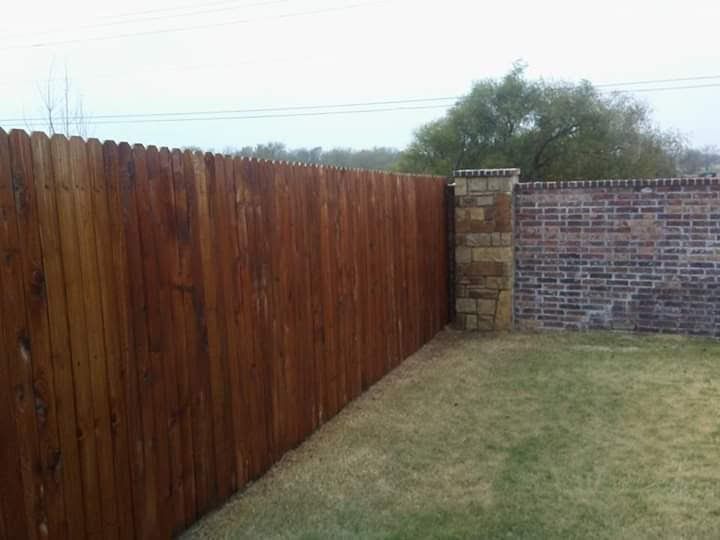 A wooden fence surrounds a brick wall in a backyard.